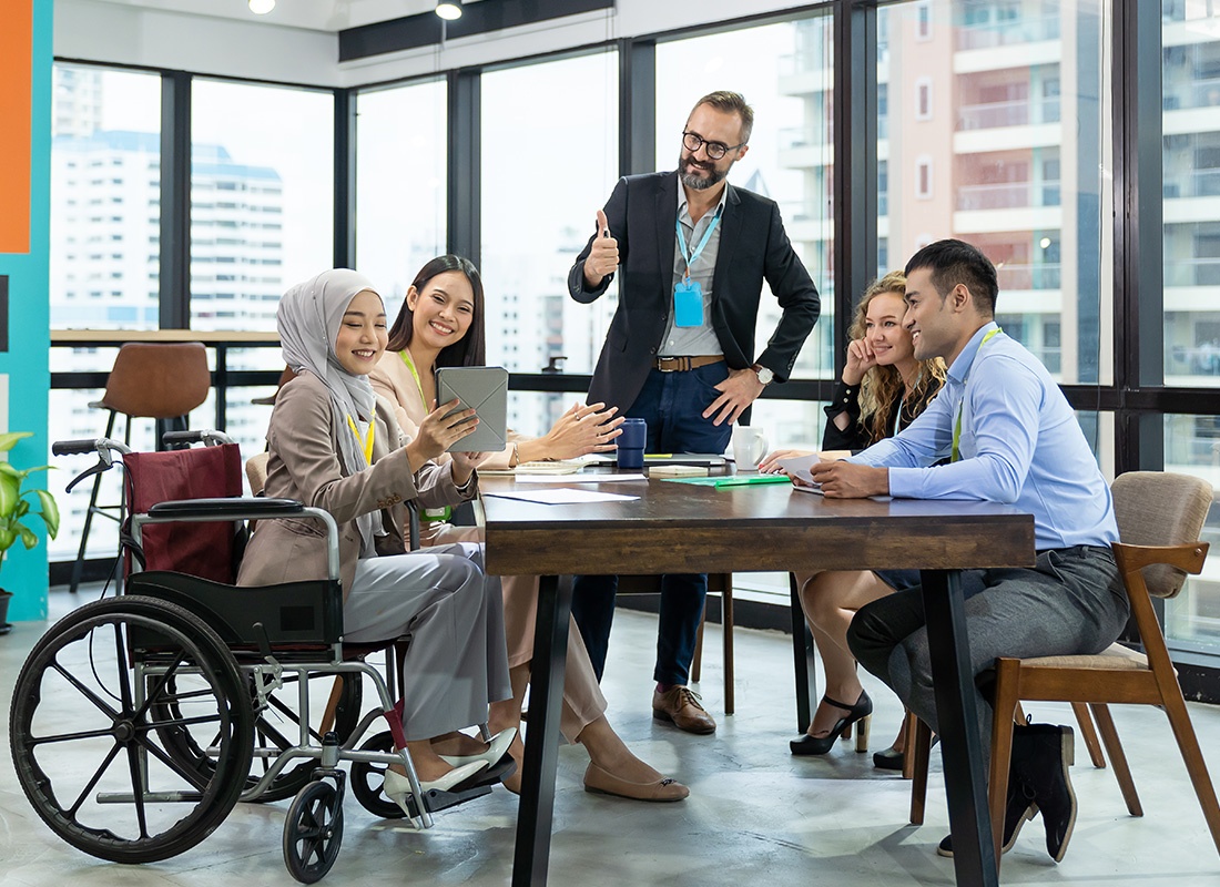 Insurance Solutions - Friendly Group of Business Professionals Have a Discussion During a Meeting While One Person in a Wheelchair Presents Some Information